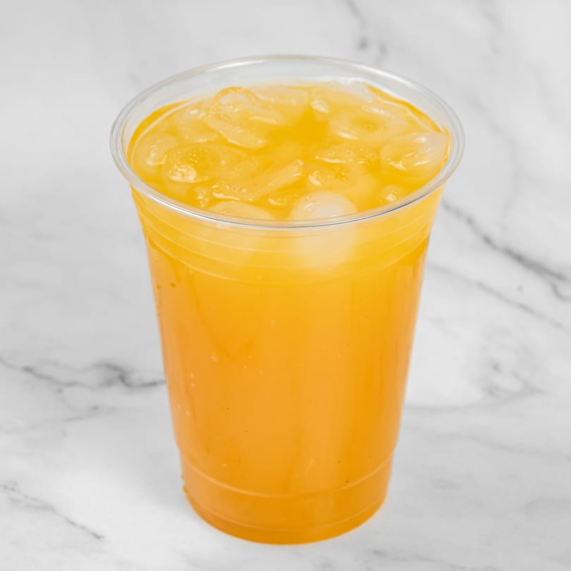 Refreshing orange juice with ice in a clear plastic cup on a white marble surface.