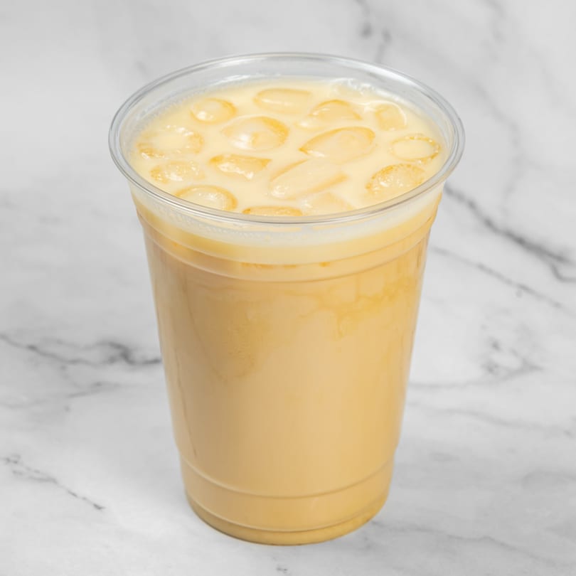 Iced coffee with milk and ice cubes in a clear plastic cup on a marble surface.