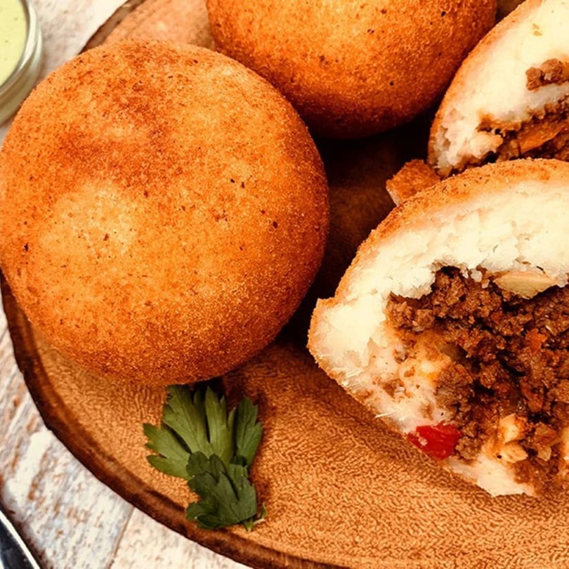 Dominican kipes, one cut open to show the savory ground beef filling, on a wooden board.