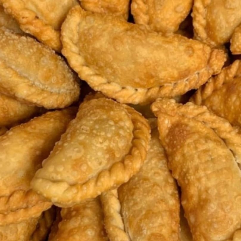Close-up of golden-brown, crispy Dominican empanadas with crimped edges, piled together.