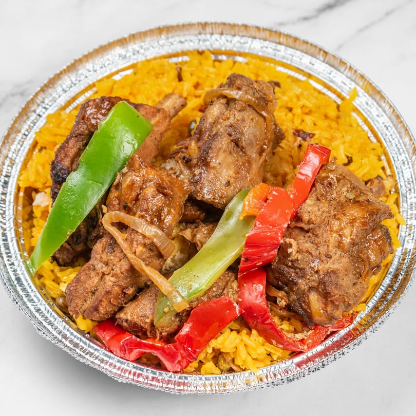 Dominican stewed chicken with yellow rice, red and green bell peppers, and onions in a foil container.