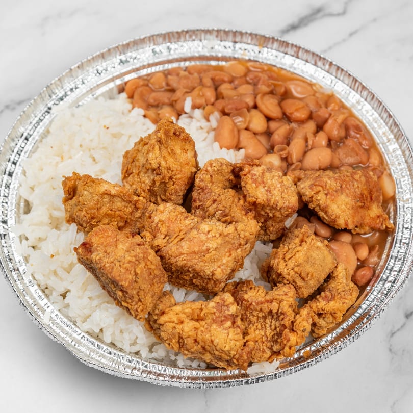 Dominican fried chicken with white rice and stewed beans in a foil takeout container.